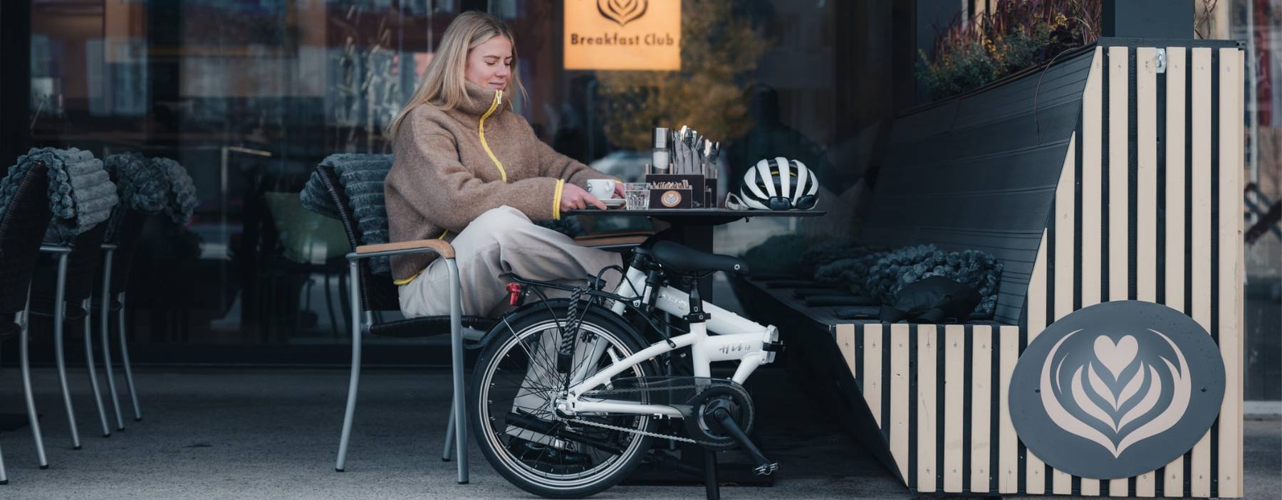 Frau sitzt mit einem zusammengefalteten DAHON Klappfahrrad vor einem Café