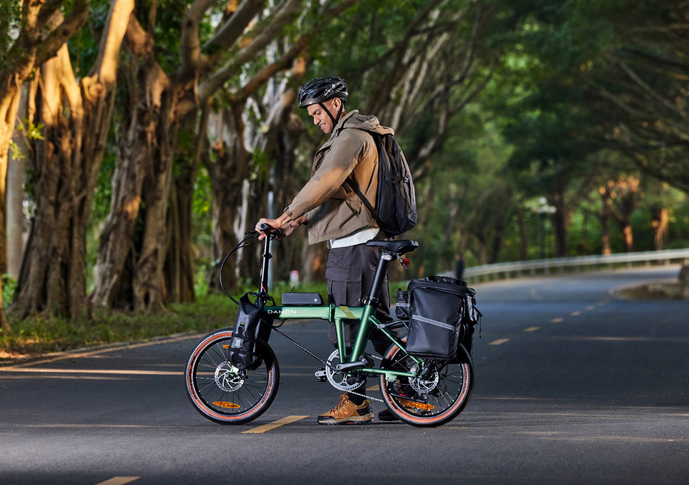 Green DAHON electric SUV bike with panniers, a man beside it on a paved road, showcasing urban portability.
