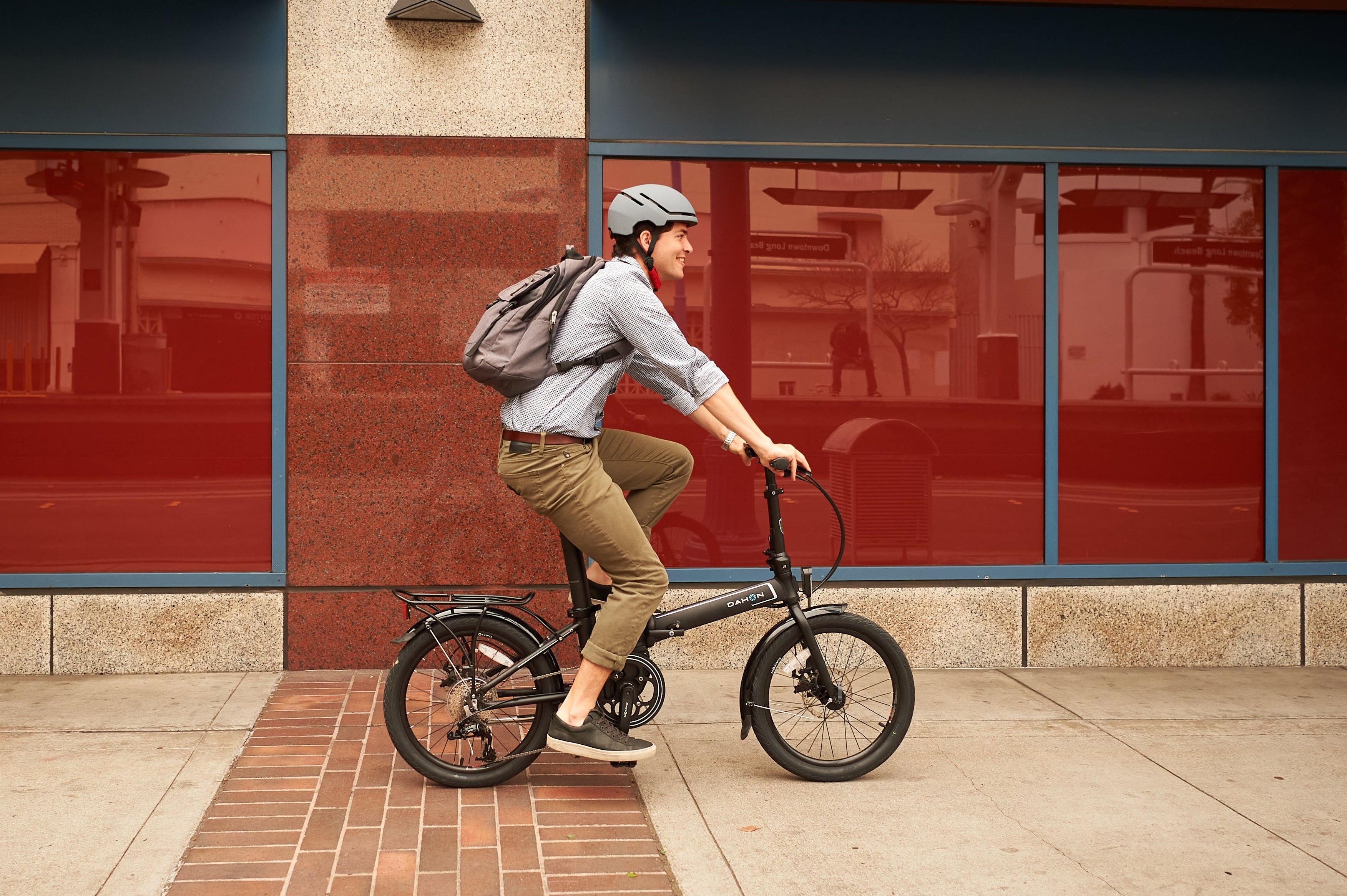 Man riding black DAHON Unio E20 foldable electric bike with mid-drive motor in urban environment.