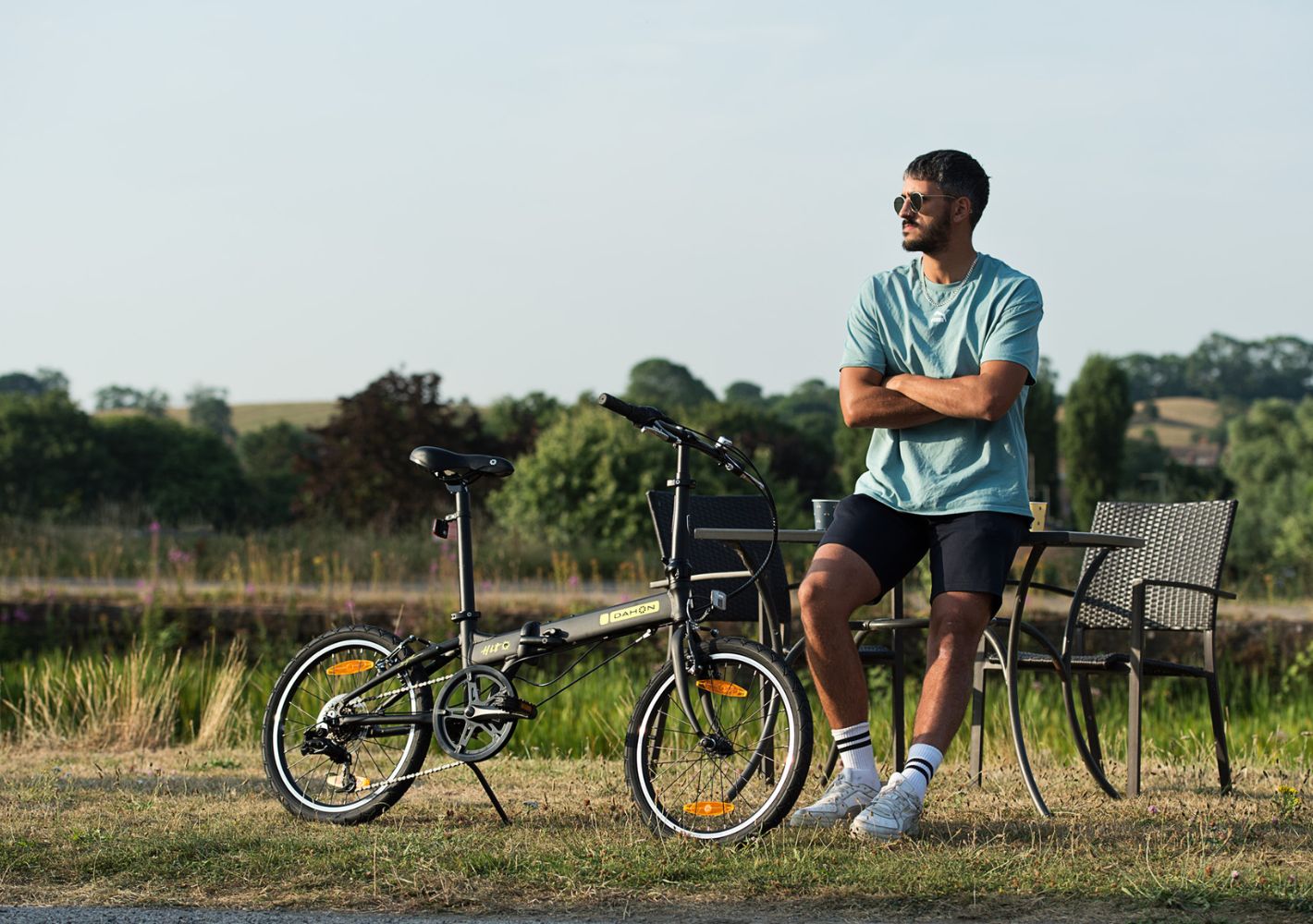 Man with Dahon HIT D6 folding bike with yellow accents, small wheels, rear rack, fenders, outdoors lifestyle shot.