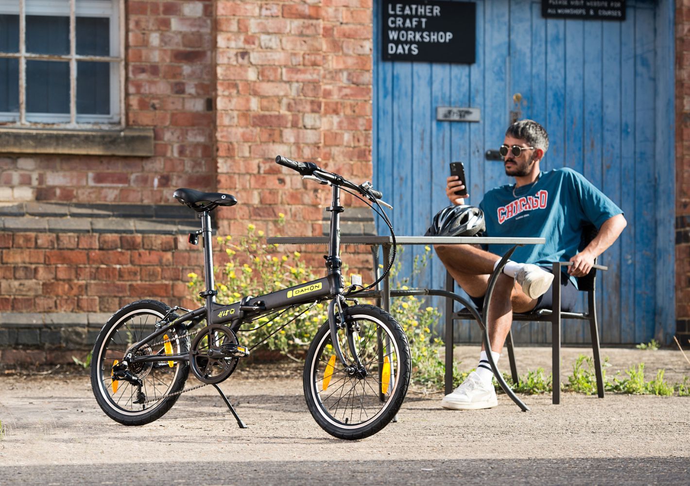 Man relaxing by black Dahon HIT D6 folding bike outside cafe, lifestyle shot. HIT D6 portability.