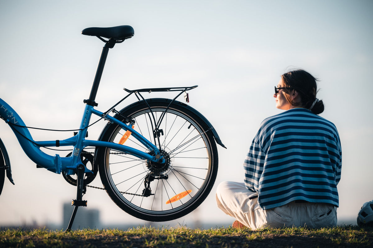 Blue folding bike parked on grass as a woman sits watching the sunset