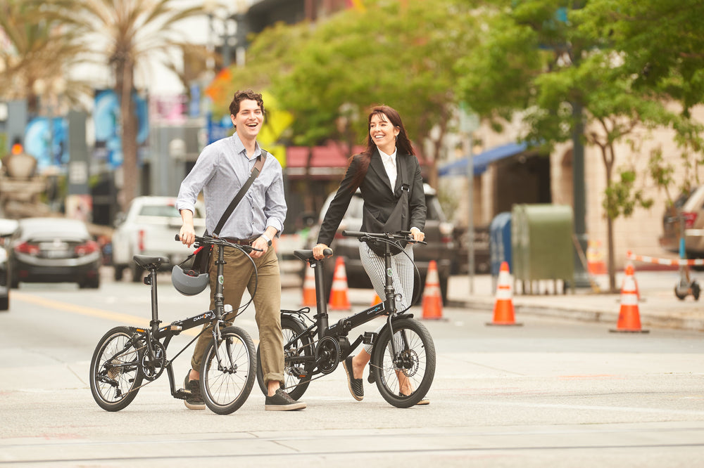 A man and a woman walk with their DAHON folding bikes on a city street, showcasing urban commuting style.