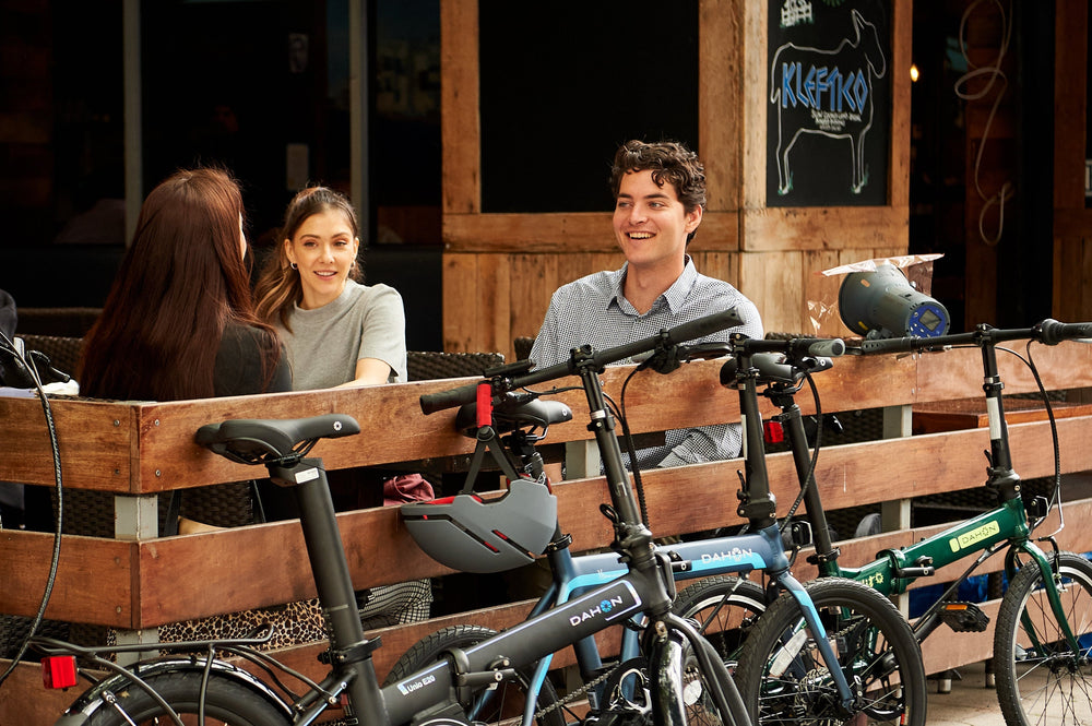 A group of friends sits on a city bench with their DAHON folding bikes parked beside them, ready for an urban adventure.