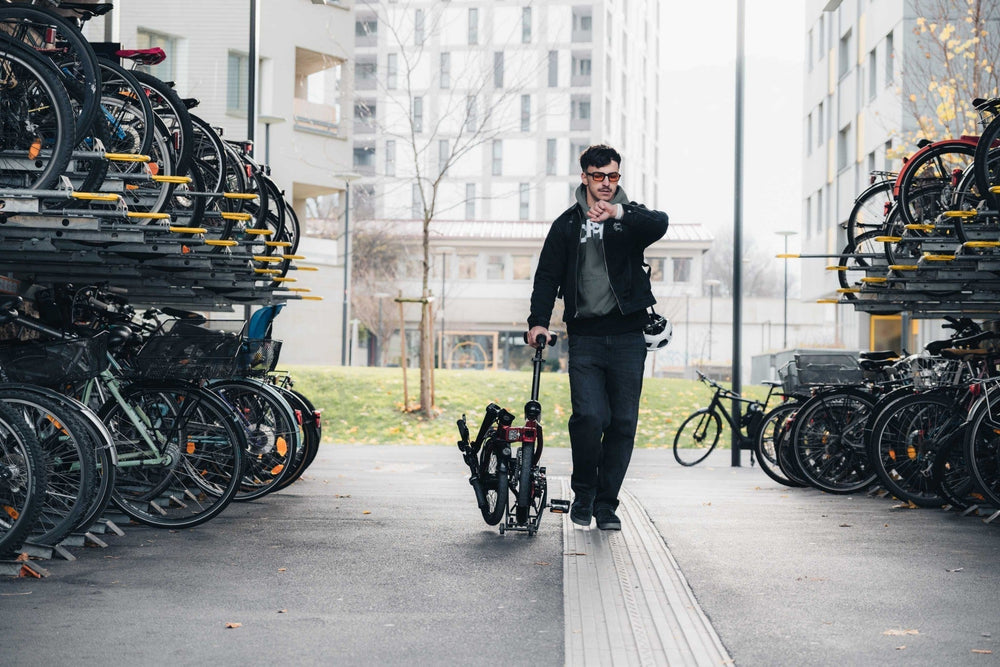 Man wheeling a folded bike through outdoor bicycle parking while checking his watch