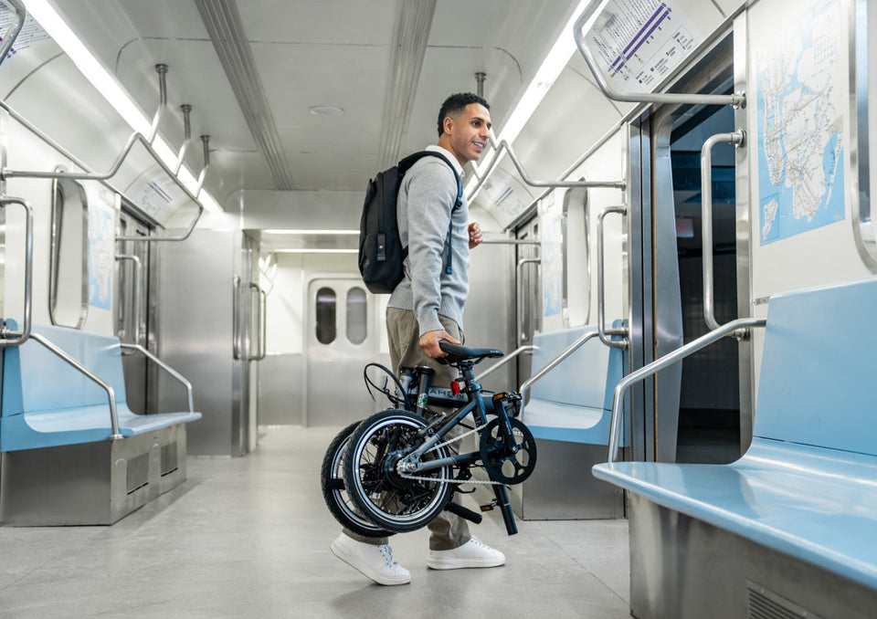 K-Feather - Man carrying folded dark blue K-Feather e-bike on a subway for urban commuting convenience.
