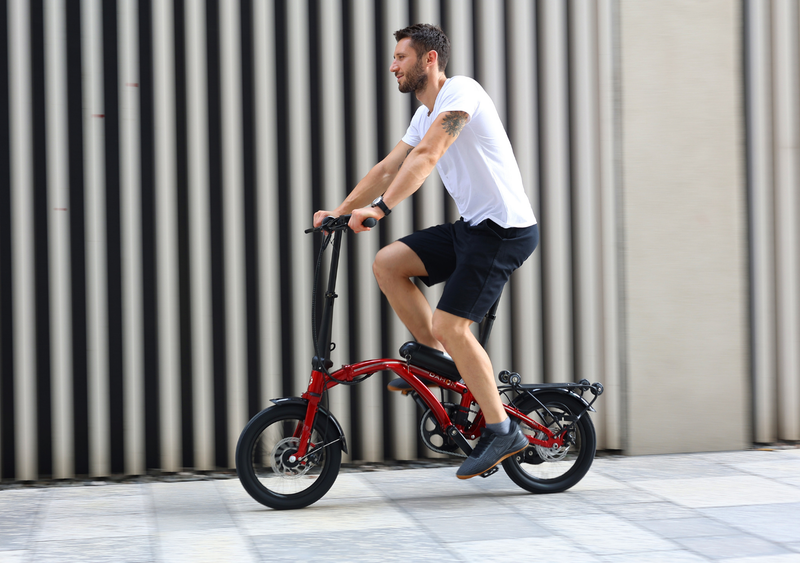 Man riding red Curl Ei4 electric trifold bicycle with black accents and rear rack.